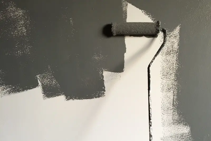 Rodillo con pintura gris sobre una pared parcialmente pintada.